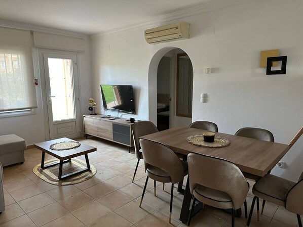 A dining area with a wooden table and chairs, a television on a cabinet, and a window with curtains.