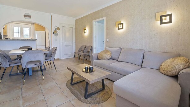 Sala de estar con sofá, mesa de centro y sillas, además de una zona de cocina con mesa y sillas, y una puerta que da a otra habitación.