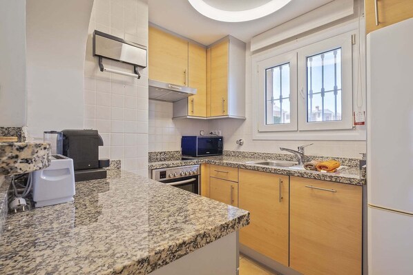 A kitchen with granite countertops, stainless steel appliances, wooden cabinets, and a window with a view.