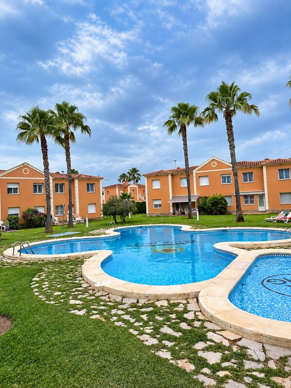 A swimming pool with a curved design, surrounded by palm trees and a building with a tiled roof.