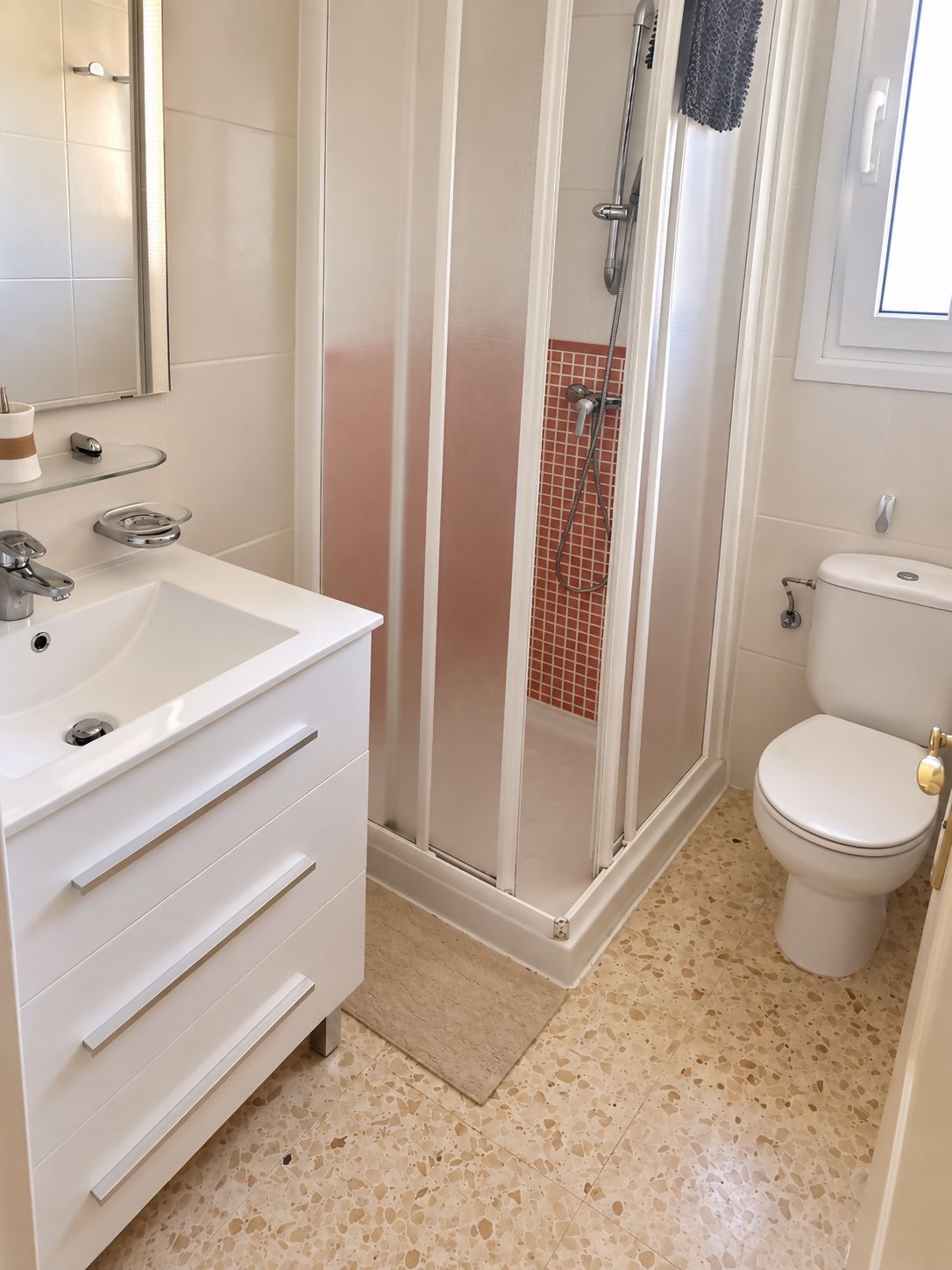 Un baño con un lavamanos blanco, un inodoro y una zona de ducha con mampara de vidrio.