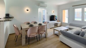 Een moderne woonkamer met een bank, een eettafel met stoelen, een televisie en een koffieapparaat.