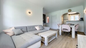 Een moderne woonkamer met een grijze bank, een witte salontafel en een eethoek met roze stoelen en een witte tafel.