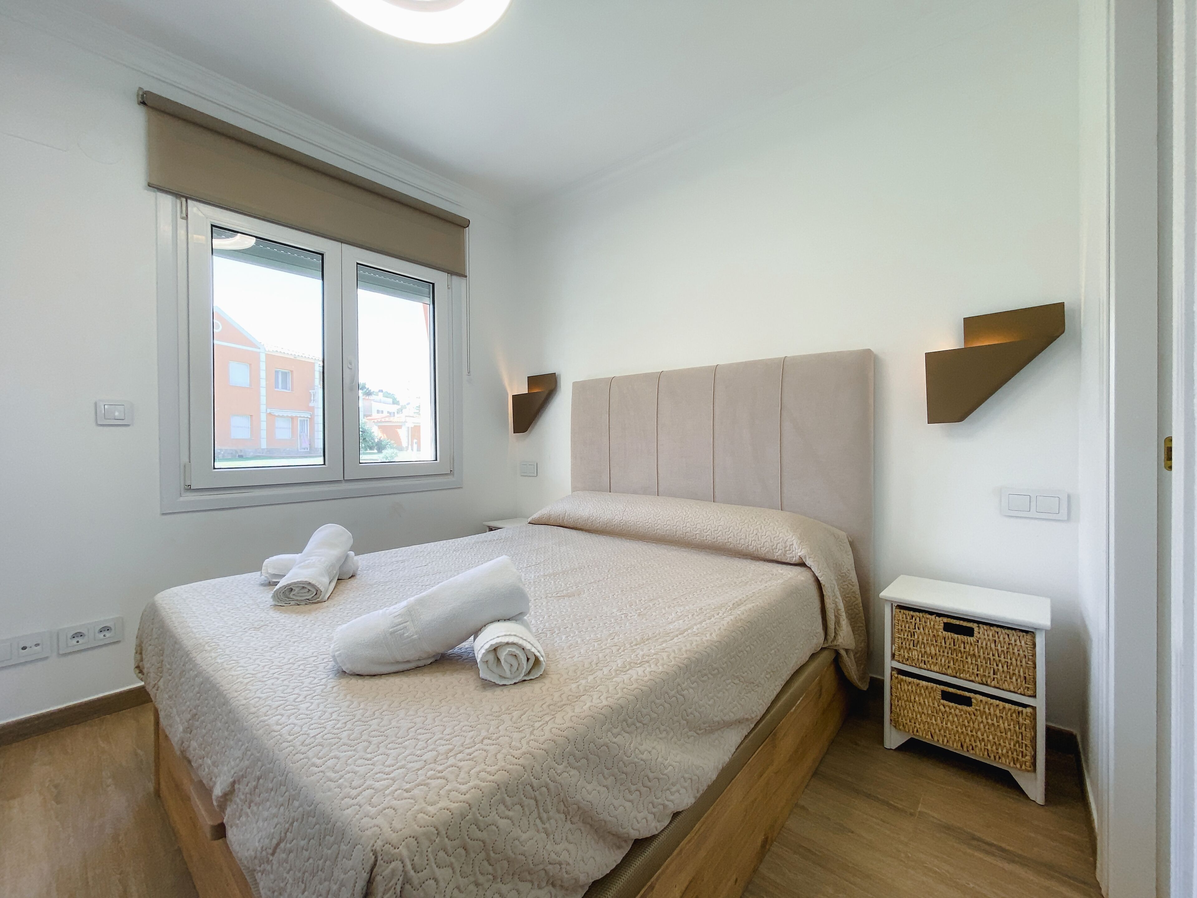 Une chambre à coucher comprenant un lit, une fenêtre, une table de chevet et un luminaire fixé au mur.