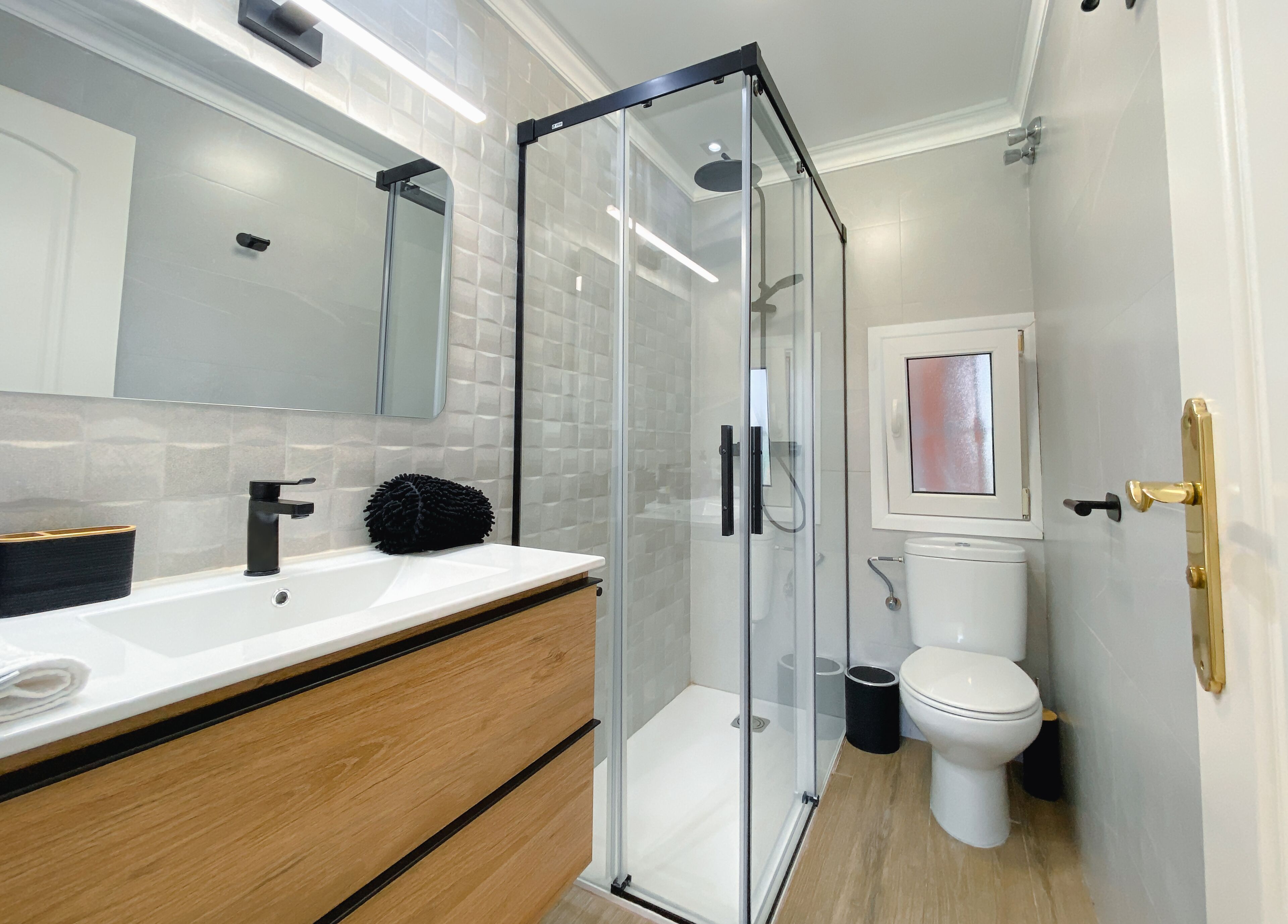 A modern bathroom with a glass-enclosed shower, a white sink with a black faucet, and a toilet with a framed picture above it.