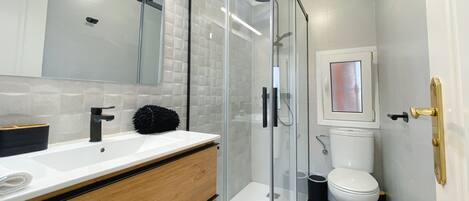 A modern bathroom with a glass-enclosed shower, a white sink with a black faucet, and a toilet with a framed picture above it.