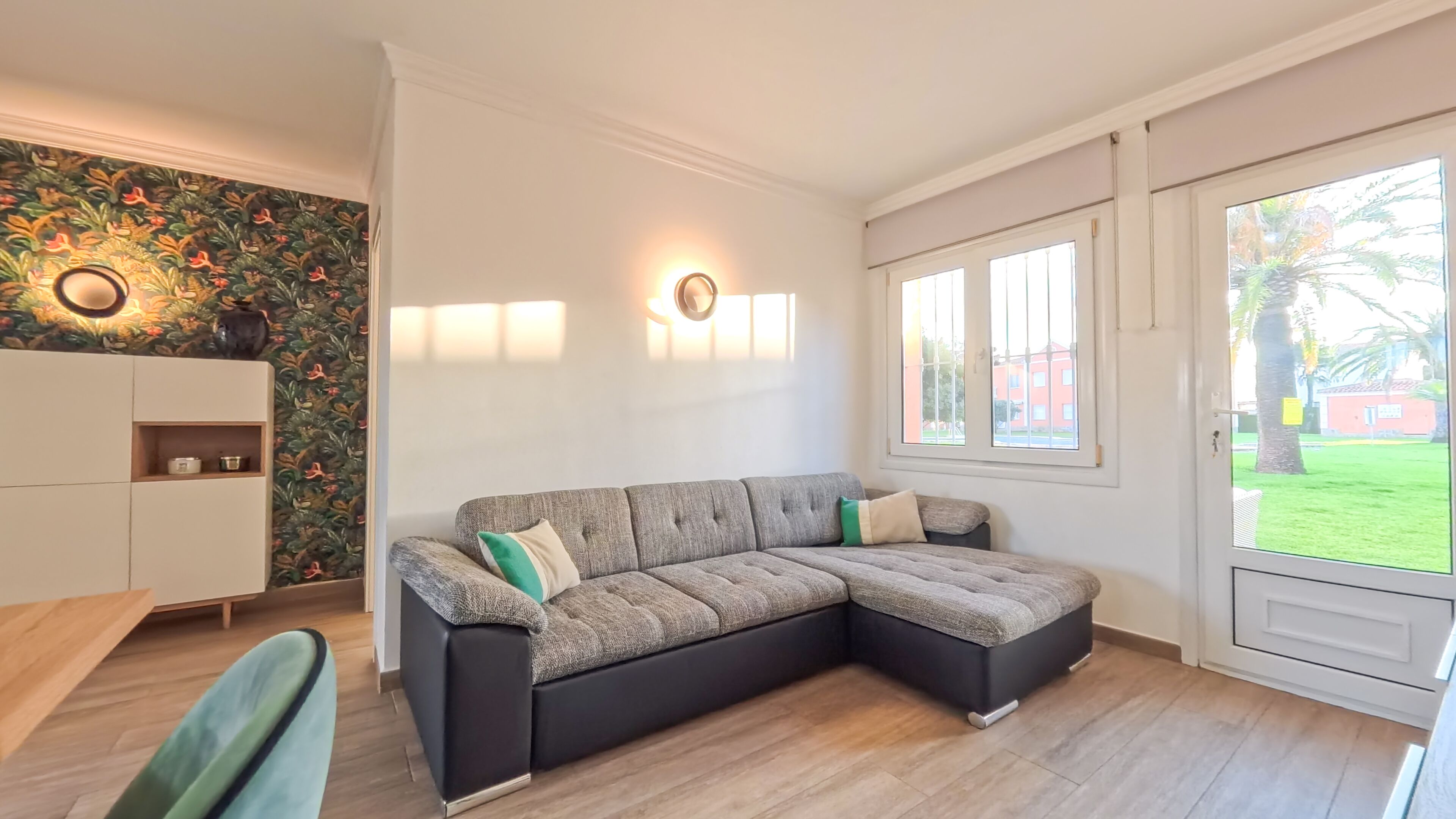 Een moderne woonkamer met een modulaire bank, een wit kastje en een groot raam met uitzicht op de omgeving.