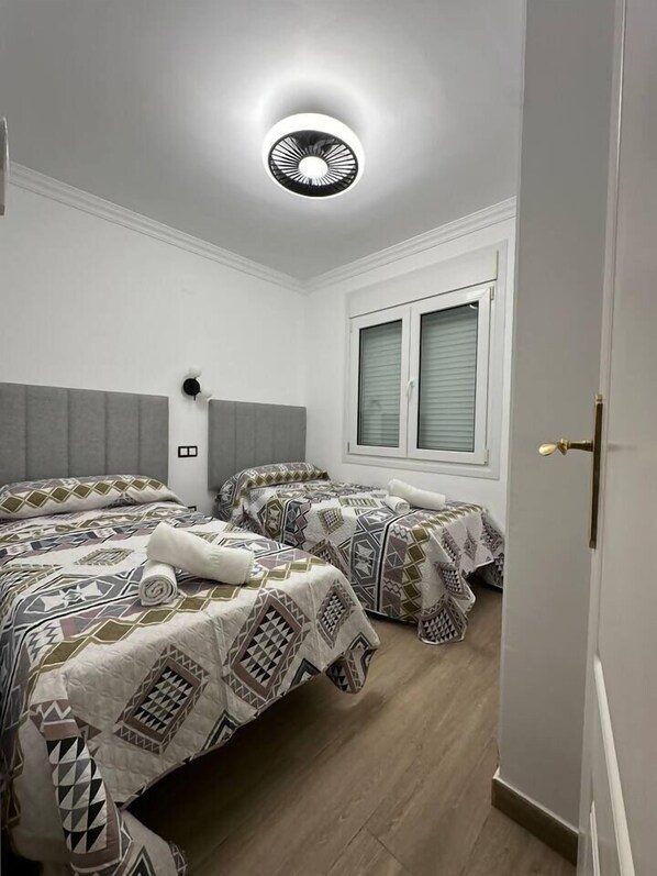 A bedroom with two beds, a window with blinds, a ceiling light, and a door.