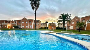 Una piscina de borde curvo, rodeada de edificios con balcones y palmeras.