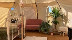 A tented room with a bed, a red sofa, and potted plants. - Flower Farm Glamping Retreat in Suffolk (Ipswich)