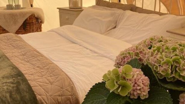 A neatly made bed with a quilted bedspread and pillows. - Flower Farm Glamping Retreat in Suffolk (Ipswich)