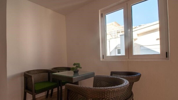 A small room with two wicker chairs, a table, and a window with a view of buildings.