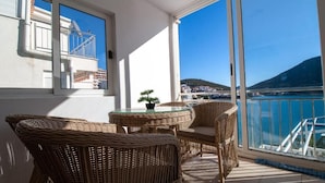 A balcony with wicker furniture and a glass table, overlooking a coastal area with buildings and a mountain. - 6 Double room with Private Parking (Neum)
