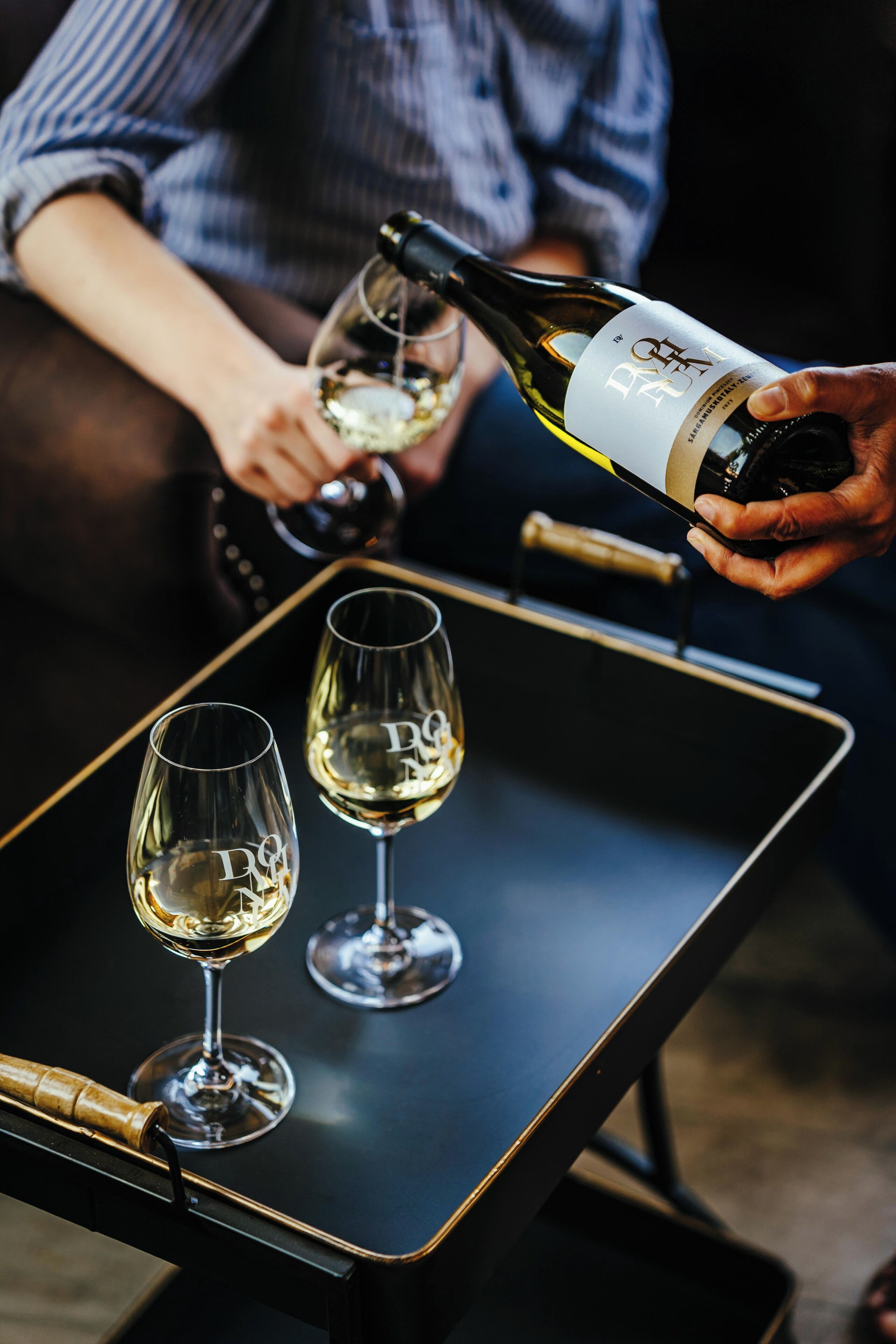 A person pouring wine into two glasses on a tray.