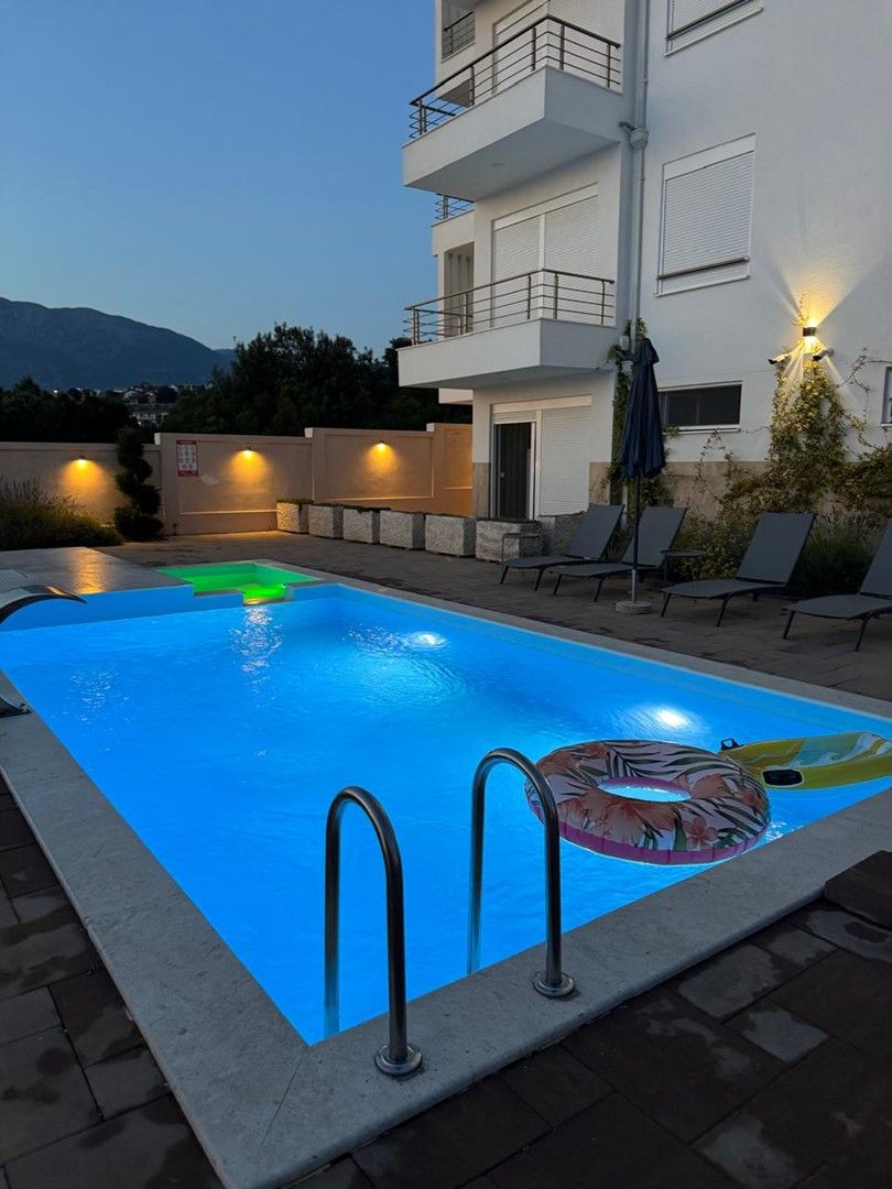 Un edificio moderno con piscina, mobiliario exterior y una vista a la montaña de fondo.