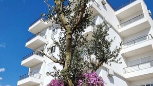 A multi-story building with balconies and a tree with purple flowers in front. - NEW! Apartment 2 with Pool in Bar, Montenegro (Bar)