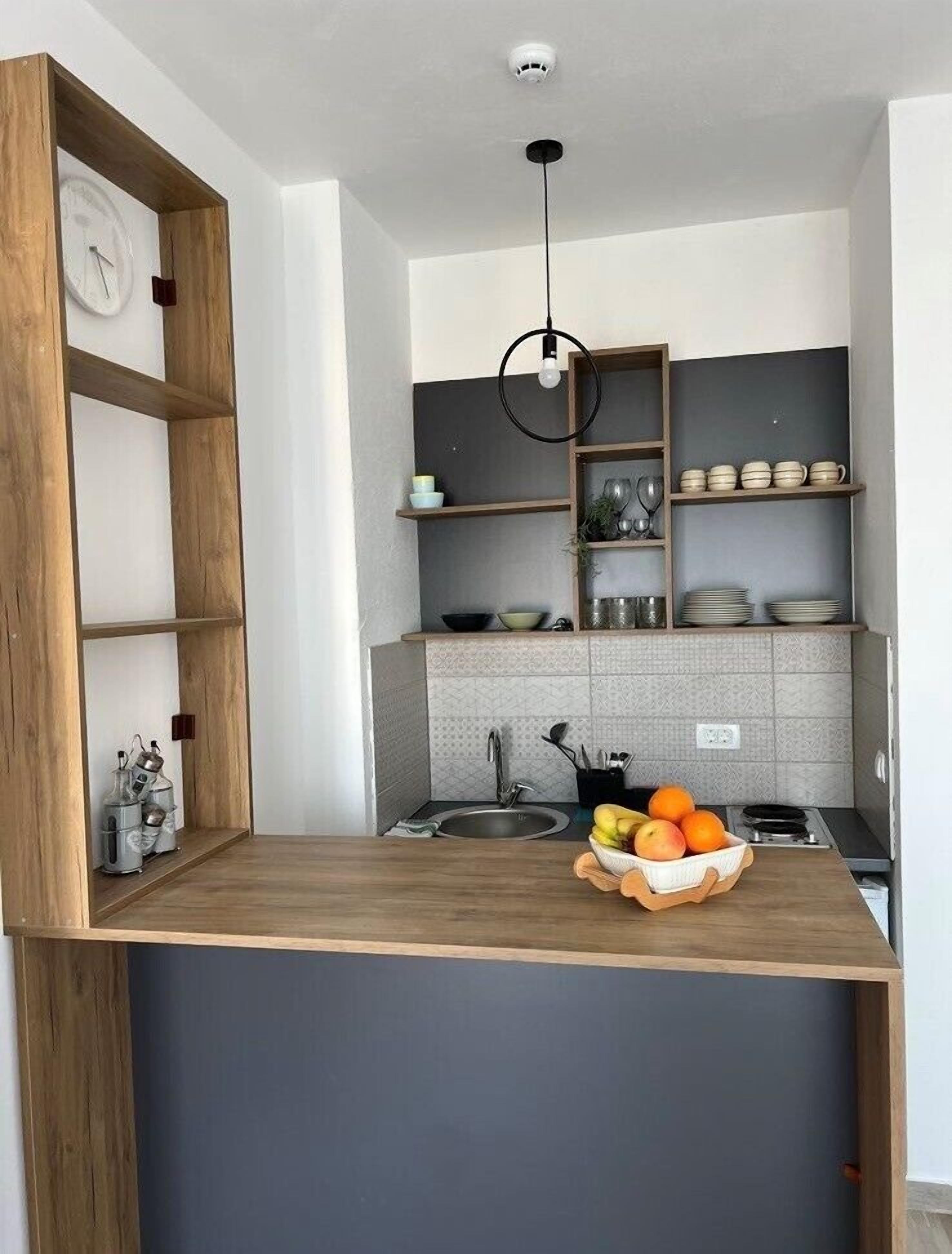 A modern kitchen with wooden shelves, a built-in clock, and a fruit bowl on the counter.