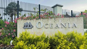 A sign with the name "Oceania" and a ship illustration, surrounded by greenery and a fence.