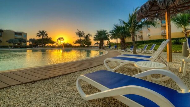 A poolside area with lounge chairs and a thatched umbrella.