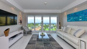 A modern living room with a large sliding glass door leading to a balcony with a view of the ocean.