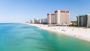 A coastal hotel with multiple high-rise buildings, a sandy beach, and clear turquoise waters.