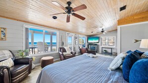 A spacious room with a large bed, a ceiling fan, a television, and a view of the ocean.