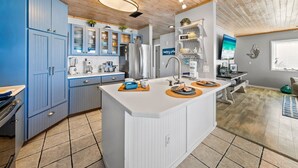 A modern kitchen with blue cabinets, a central island, and a wooden ceiling.