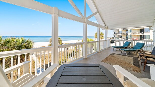 A balcony with a view of the beach, lounge chairs, and a table.