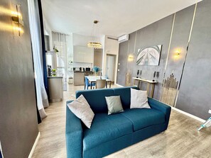 Un salon moderne avec un canapé de couleur turquoise, un coin repas et une cuisine en arrière-plan.