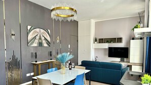 Ett modernt vardagsrum med en blå soffa, ett matbord med stolar, en kristallkrona och en tv som är monterad på väggen.