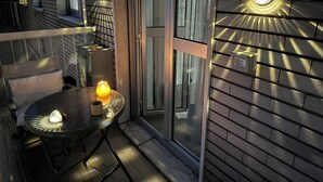 En modern utomhusplats med sittmöbler, bestående av ett glasbord och stolar, ett litet bord med ett ljus och en väggmonterad lampa.