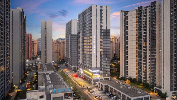 Hotel moderno e alto, com vários andares, área de estacionamento e vista para a rua.