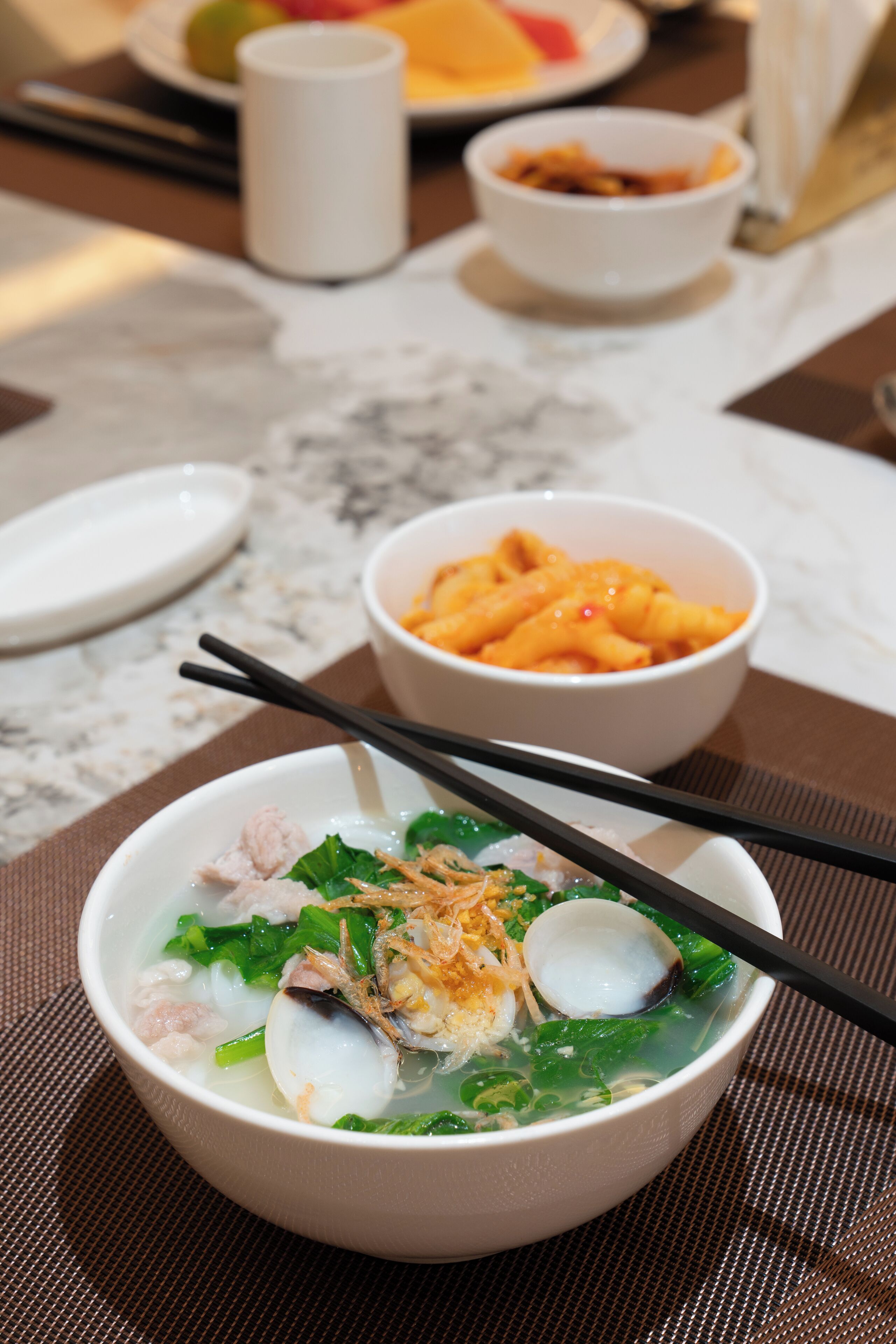 A bowl of soup with chopsticks on a table with other dishes.