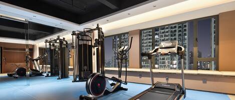 Un gimnasio moderno con diversos equipos de ejercicio, amplias ventanas con vista a la ciudad y suelo azul.