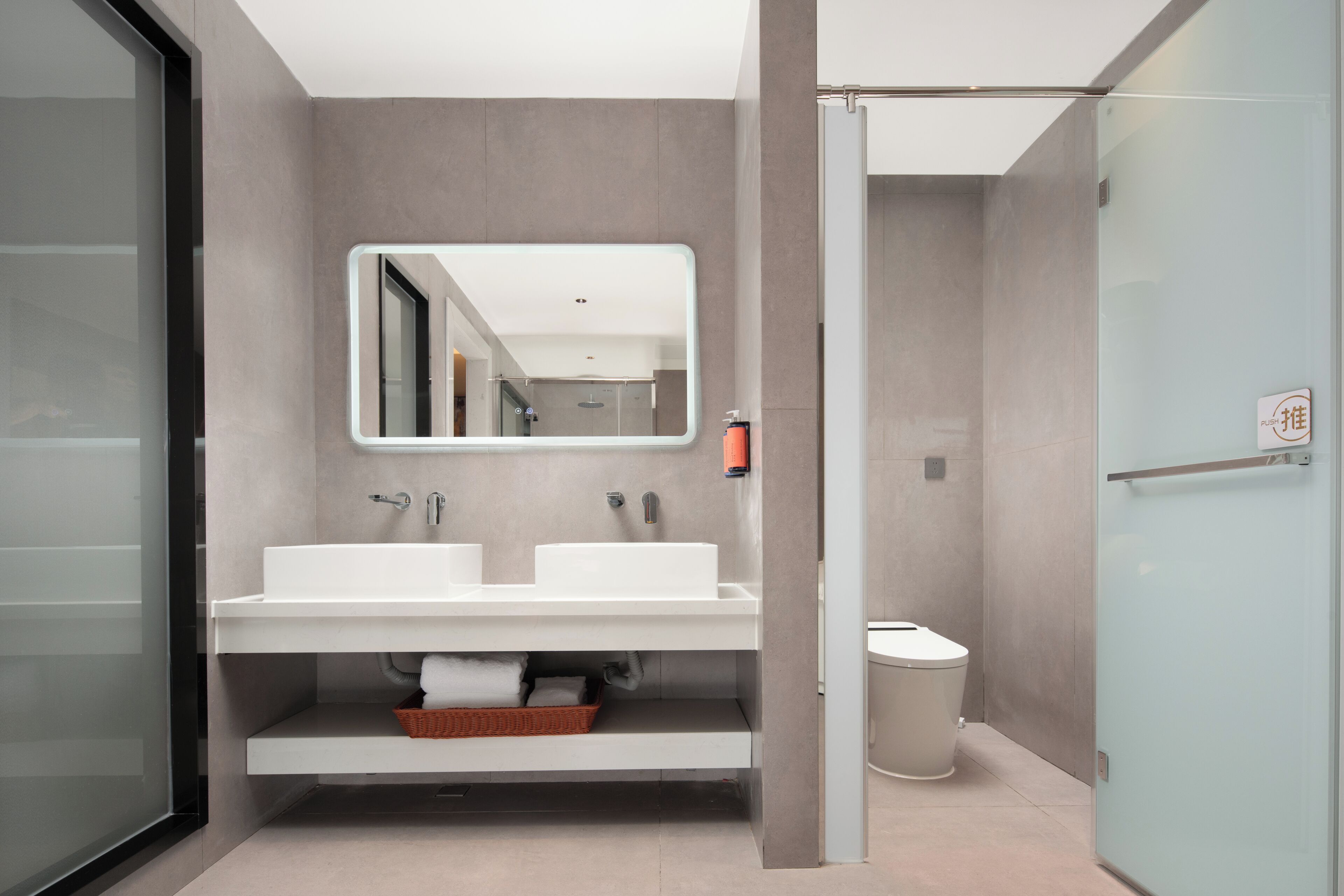 Une salle de bain moderne avec une douche à parois de verre, un grand miroir et un lavabo blanc avec un panier en dessous.