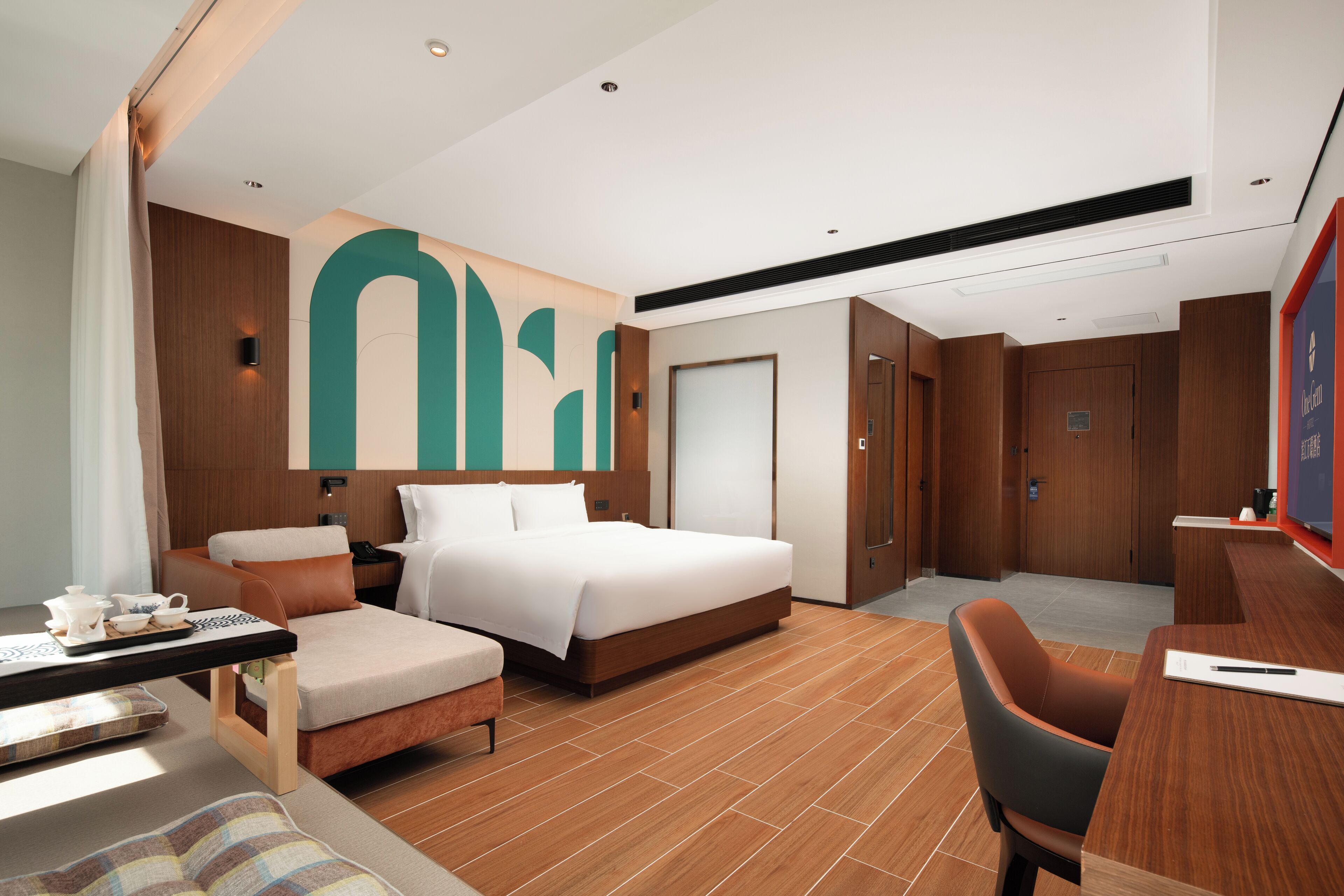 A modern hotel room with a large bed, a desk, a chair, and a large abstract wall art piece.