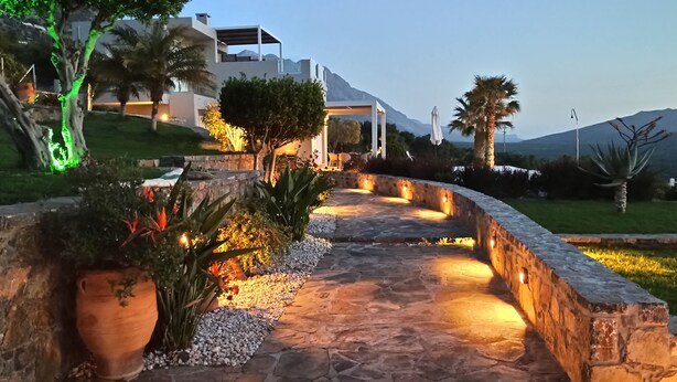 A stone pathway with potted plants and a well-lit outdoor area. - Luxurious Villa Tholos Crete (Ierapetra)