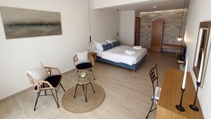 A modern bedroom with a large bed, a small dining area, and a seating area with wicker chairs. - Luxurious Villa Tholos Crete (Ierapetra)