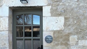 A stone building with a green door, a small sign above the door, and a lantern on the wall.