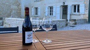 A bottle of Chateauneuf-Montrachet wine and two glasses on a wooden table with a stone building in the background.