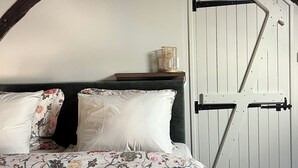 A bedroom with a bed, floral bedding, a wooden headboard, a white door, and exposed wooden beams.