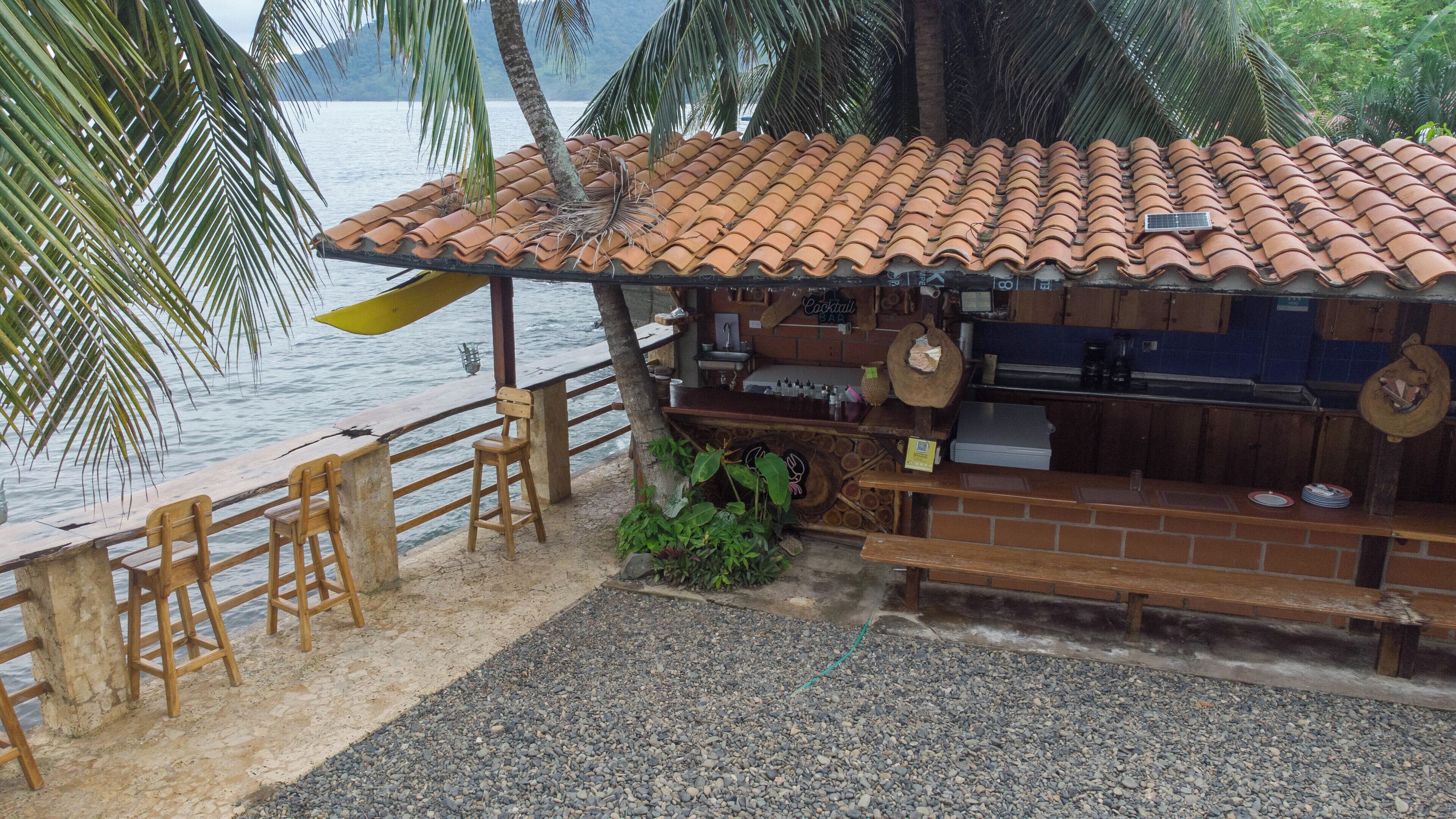 A beachside bar with a tiled roof, wooden furniture, and a view of the sea.