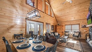 Een houten chalet van binnen met een eethoek, een zithoek en een open haard.