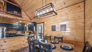Een houten chalet van binnen met een keuken, een eethoek en een slaapkamer op een entresol.