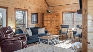 Een gezellig interieur van een chalet met houten plafond, een bank, een fauteuil en een eettafel.