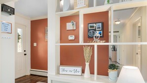 A hallway with a white door, a welcome sign, a sign reading "This is Us", a small potted plant, and a wall-mounted thermostat. - The Jolly Rancher (Slatington)