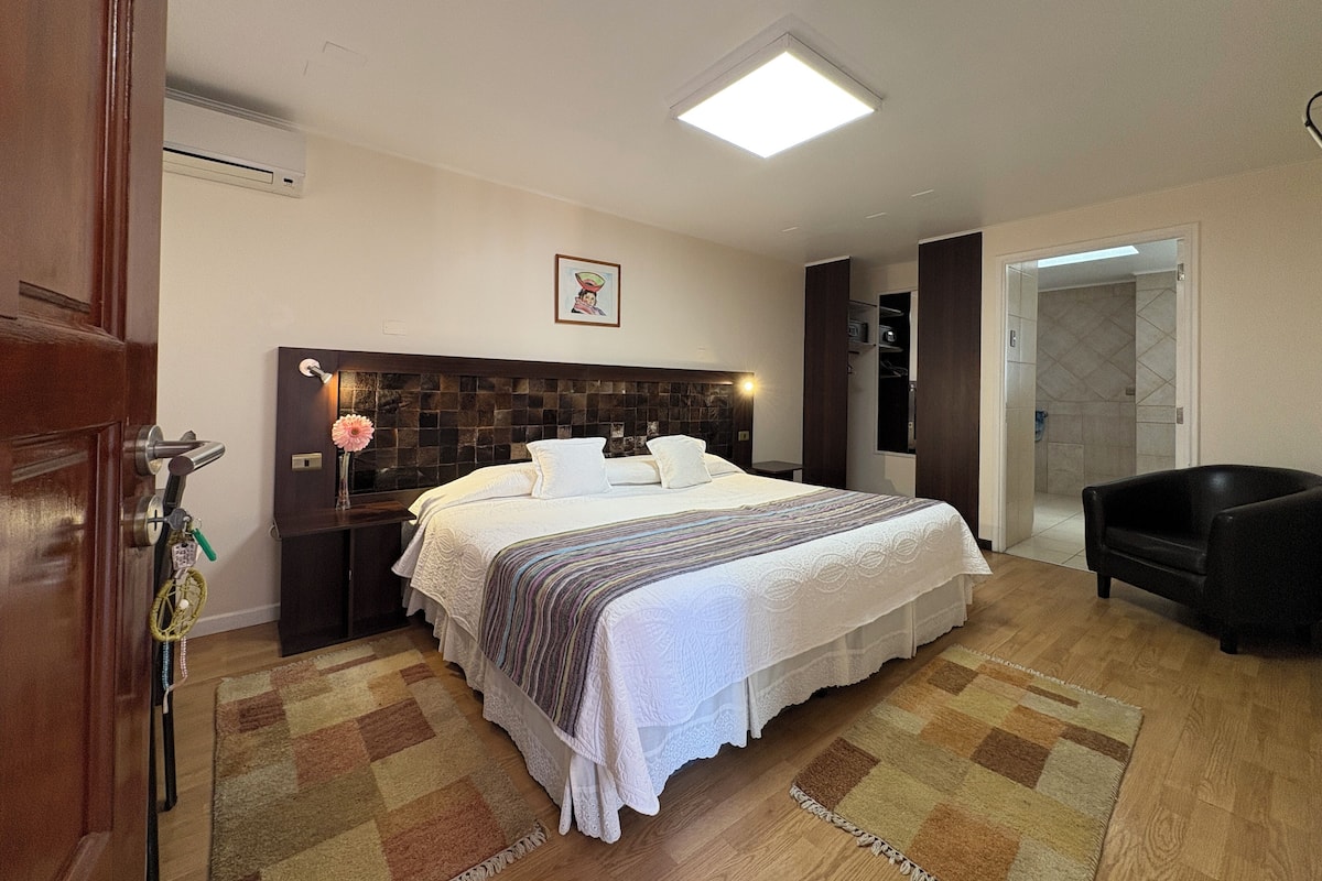 A neatly arranged bedroom with a large bed, a bedside table with a lamp, a chair, and a wardrobe.