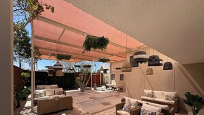 A covered outdoor seating area with wicker furniture, a table, and hanging plants. - Atankalama (Calama)