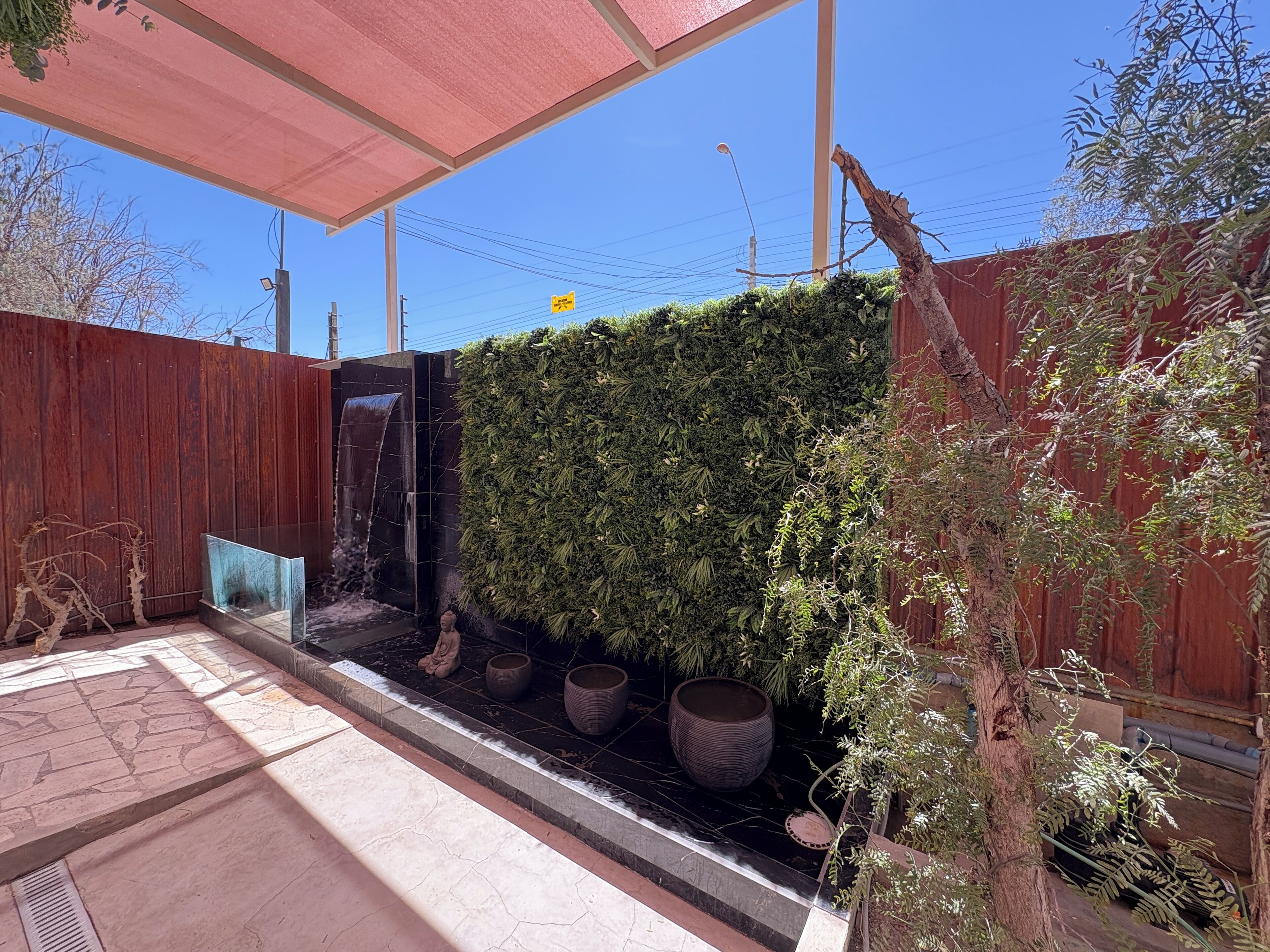 Un espacio exterior moderno con una fuente de agua, un jardín vertical y una valla de madera.