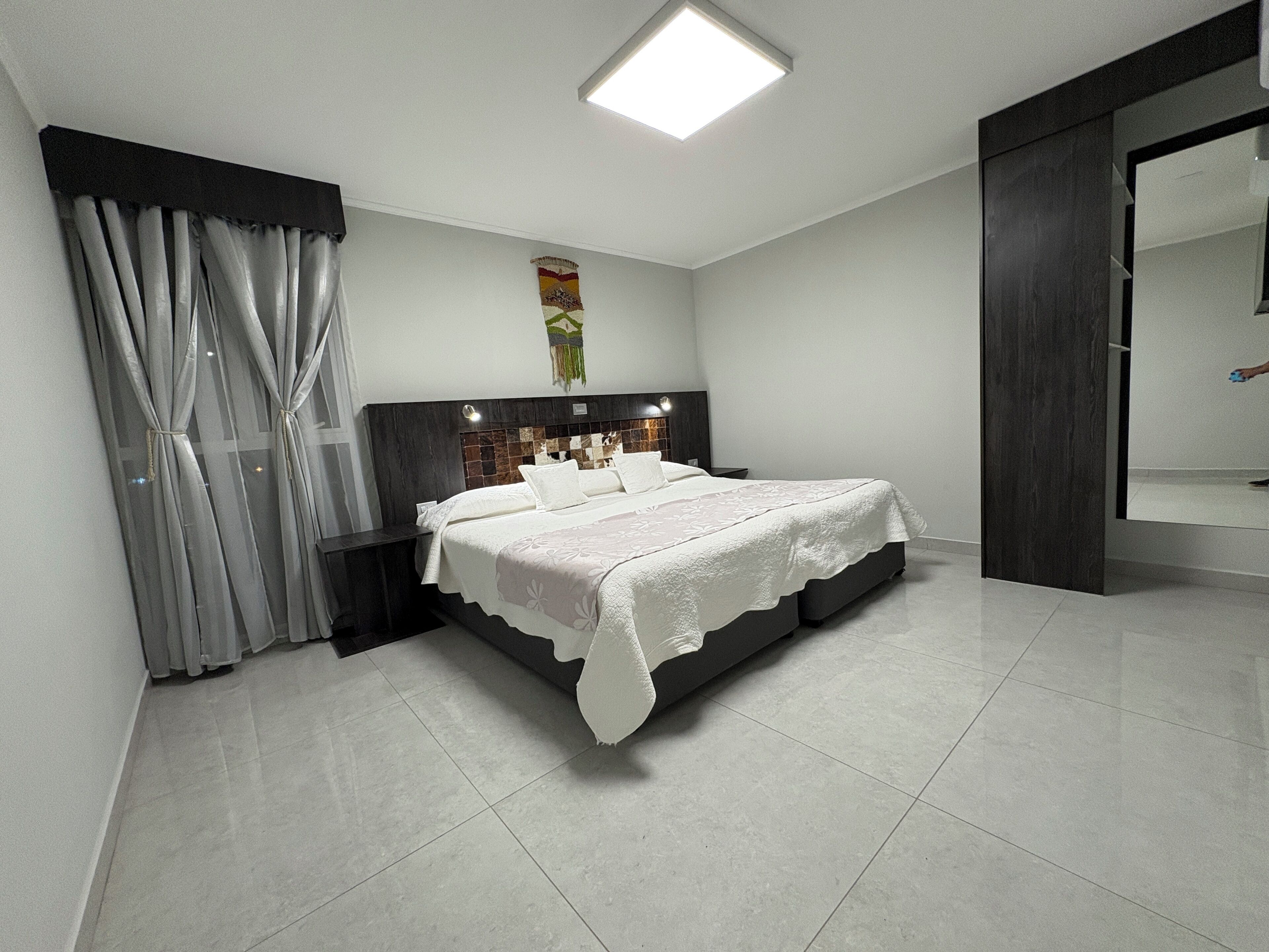 Un dormitorio moderno con una cama grande, un cabecero con panel decorativo, una lámpara de techo y un espejo amplio.